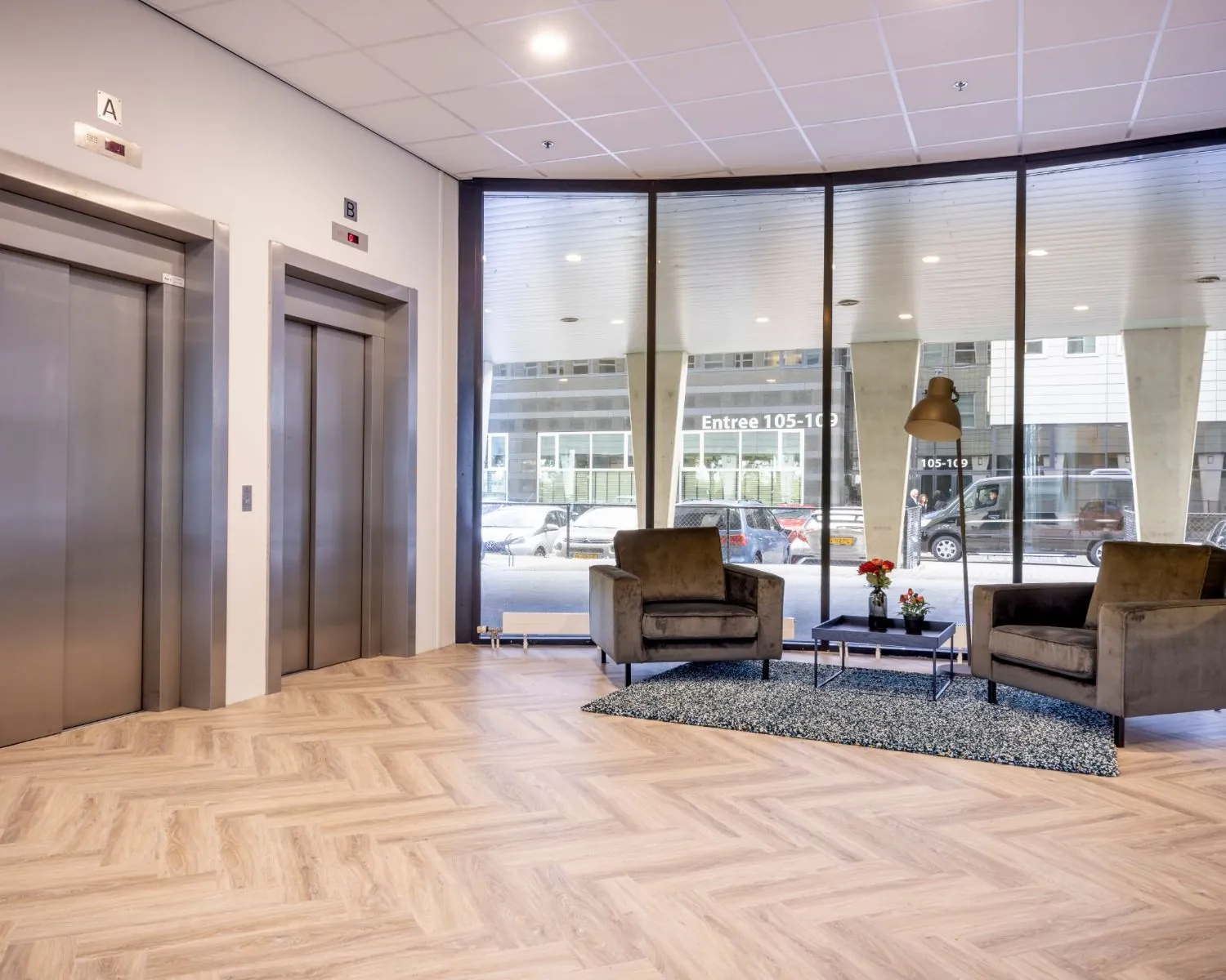 Moderne entree van een kantoorruimte aan de Tupolevlaan met zithoek, grote ramen en twee liften.
