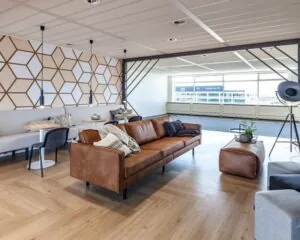 Moderne en stijlvolle kantoorruimte aan de Tupolevlaan 73 met een zithoek, vergadertafels en grote ramen voor natuurlijk licht.