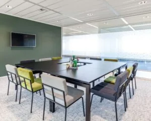 Moderne vergaderruimte met grote zwarte tafel, kleurrijke stoelen en glazen wand in kantoor aan de Tupolevlaan 73.