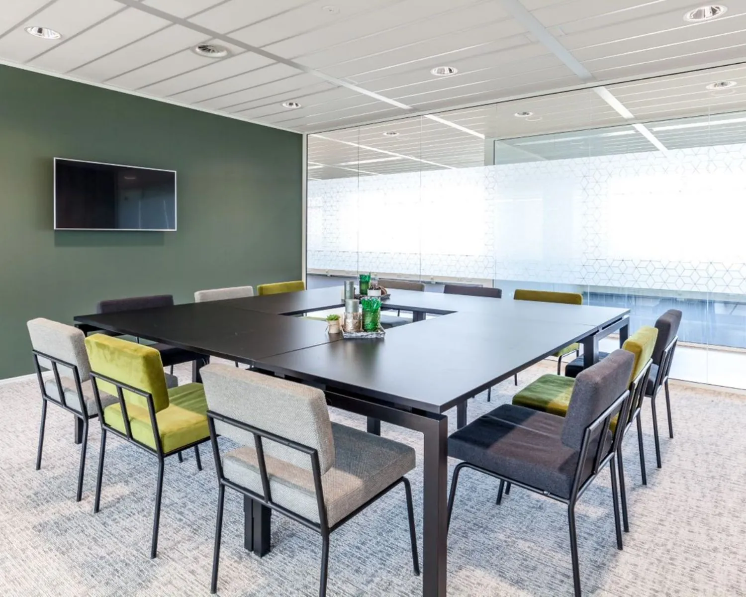 Moderne vergaderruimte met grote zwarte tafel, kleurrijke stoelen en glazen wand in kantoor aan de Tupolevlaan 73.