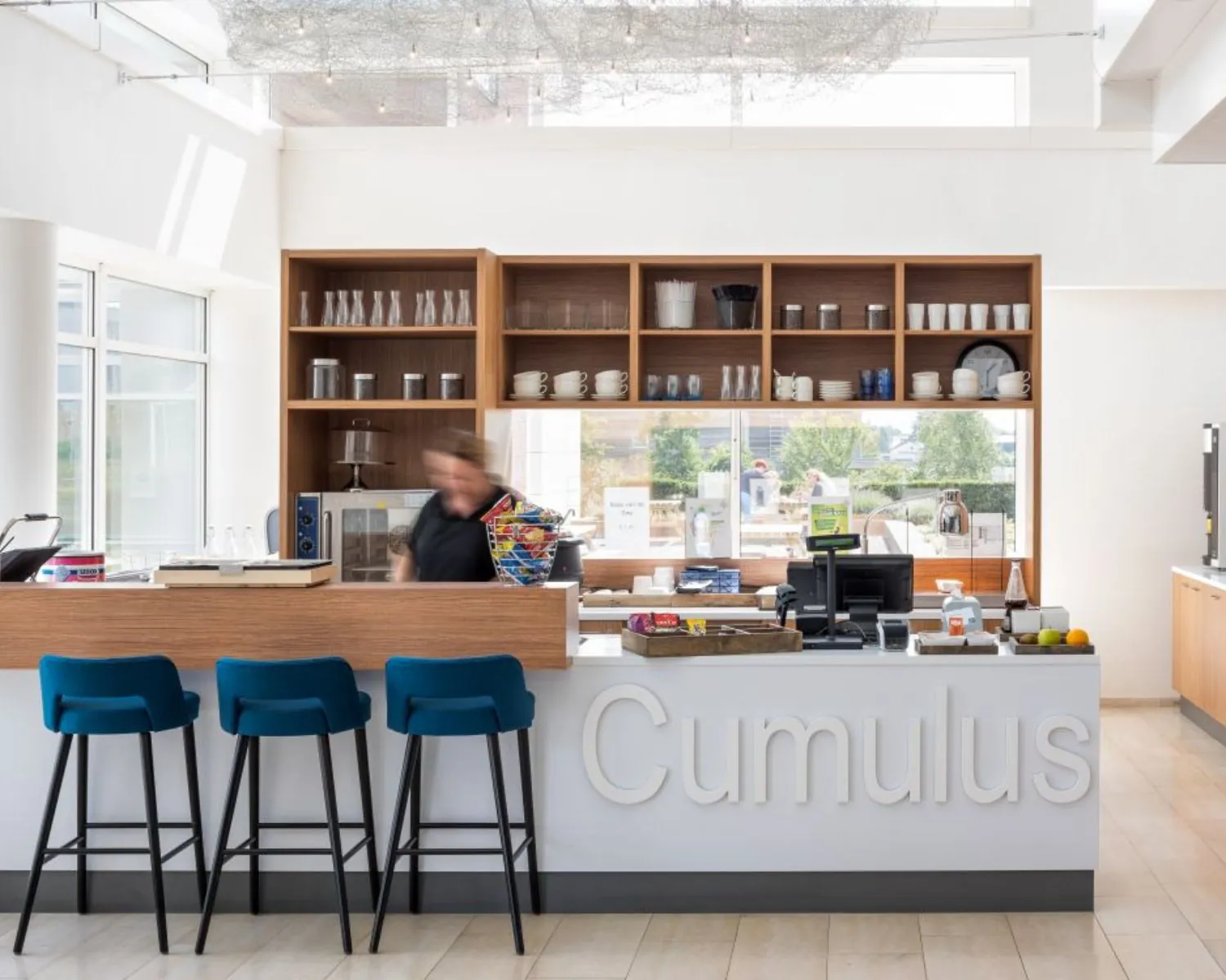 Moderne koffiebar met de naam 'Cumulus' in een kantoorruimte aan de Tupolevlaan 73, met houten accenten en blauwe barkrukken.