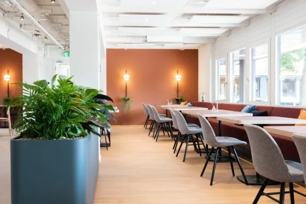 Moderne kantoorruimte met lange werktafels, grijze stoelen, planten en grote ramen aan de Atoomweg 50 in Utrecht.