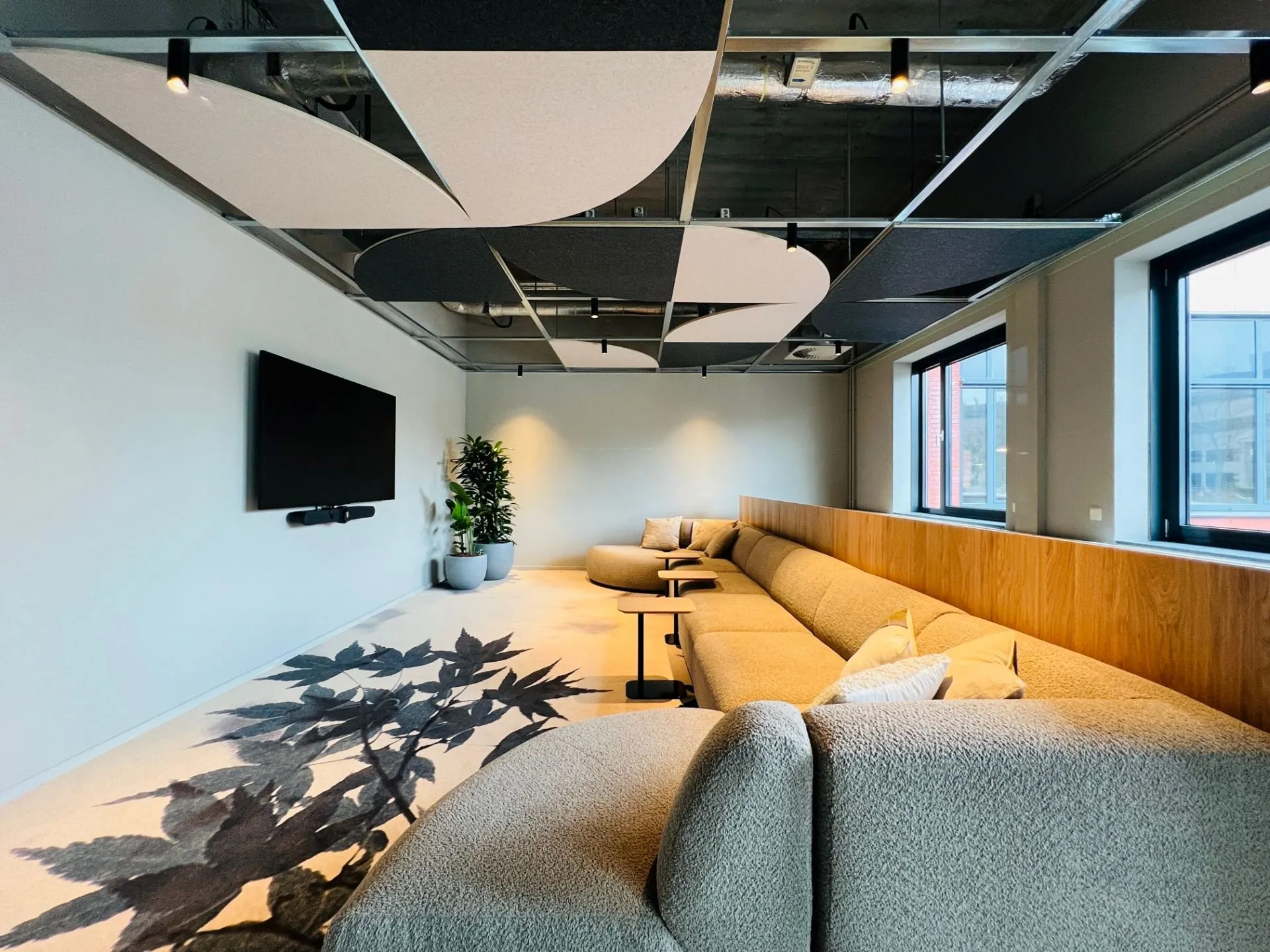 Moderne loungehoek met lange zithoek, groot scherm en designplafond in kantoorruimte aan de Varrolaan 100 in Utrecht.