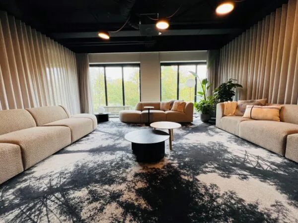 Moderne loungehoek in een kantoorruimte aan de Varrolaan 100 in Utrecht, met beige banken, ronde salontafels en grote raampartijen.