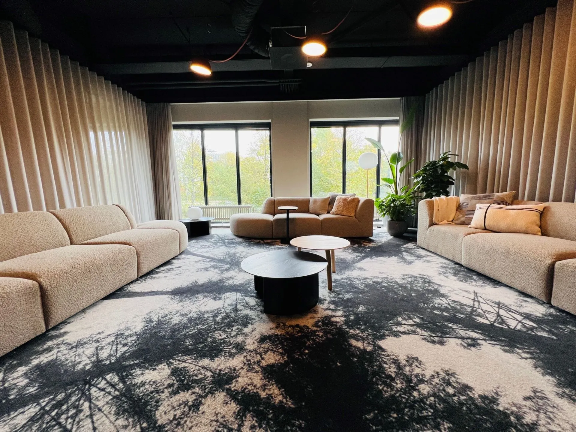 Moderne loungehoek in een kantoorruimte aan de Varrolaan 100 in Utrecht, met beige banken, ronde salontafels en grote raampartijen.
