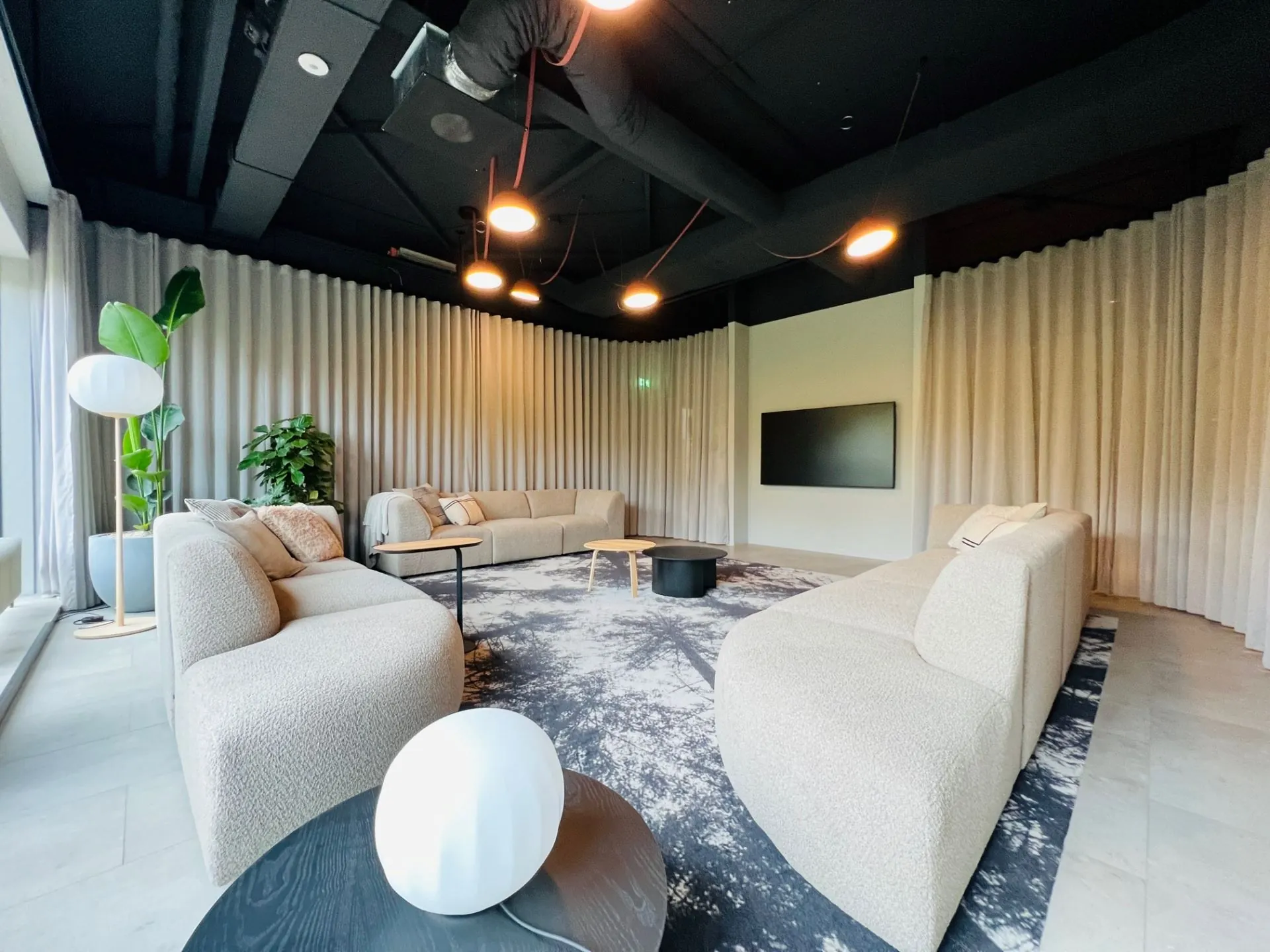 Moderne loungehoek in kantoorruimte aan de Varrolaan 100 in Utrecht met designmeubels, grote planten en een flatscreen.