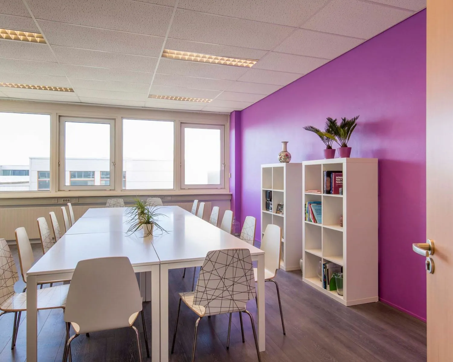 Moderne kantoorruimte aan de Waarderweg 19 met witte vergadertafel, designstoelen en paarse accentmuur.
