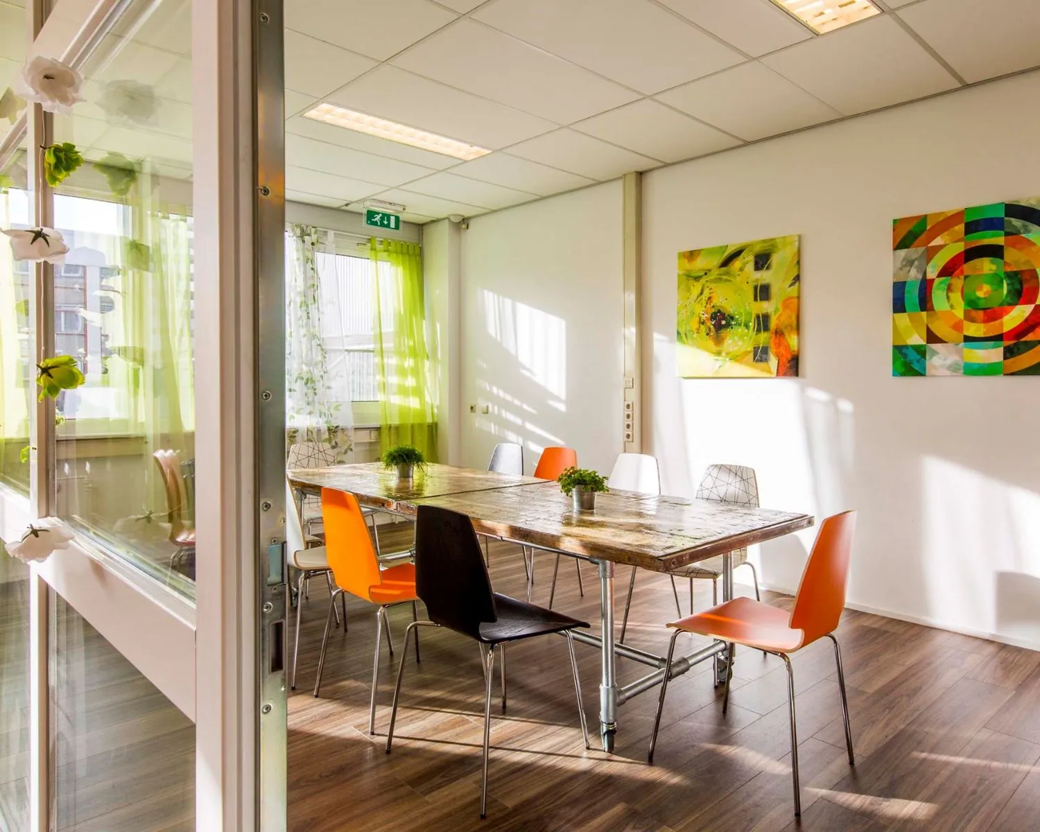 Vergaderruimte met kleurrijke stoelen, houten tafel en moderne kunst aan de muur in kantoorruimte aan de Waarderweg 19-7.