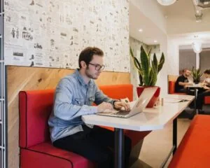Man werkt op een laptop in een moderne kantoorruimte met rode banken aan de Weteringschans 165.