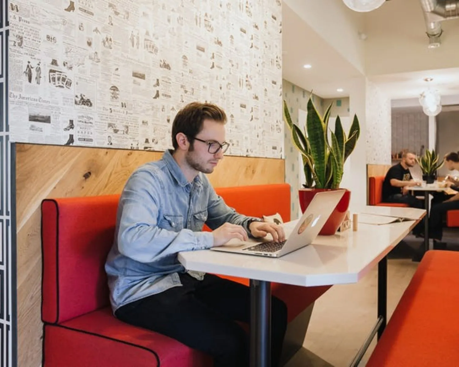Man werkt op een laptop in een moderne kantoorruimte met rode banken aan de Weteringschans 165.