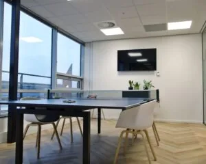 Moderne kantoorruimte aan het Bos en Lommerplein met een tafeltennistafel, witte stoelen, planten en een flatscreentelevisie aan de muur.