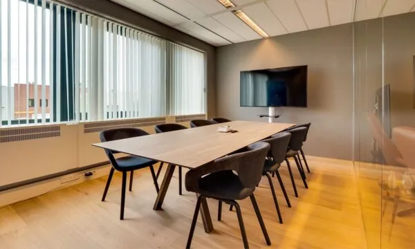 Moderne vergaderruimte met houten tafel, acht stoelen en een flatscreen-tv in kantoorruimte aan de Heerbaan 14 in Breda.