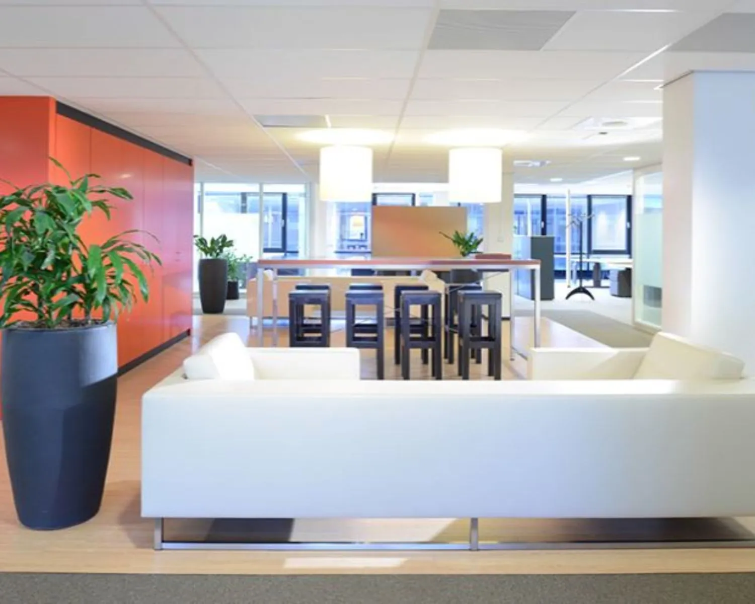 Moderne kantoorruimte met witte zitbanken, hoge tafel met krukken en oranje wand in Elisabethhof 21-23.