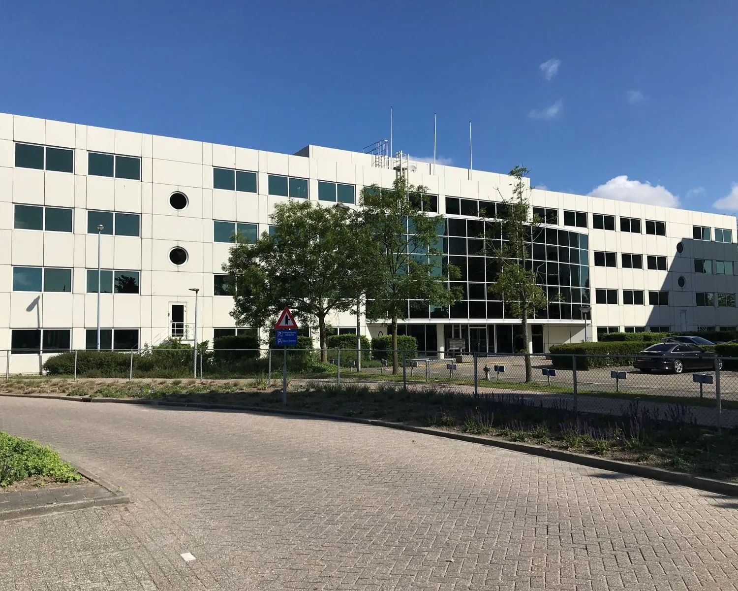 Modern kantoorgebouw aan de Haagse Schouwweg 8 met glazen entree en omringende parkeerplaatsen.