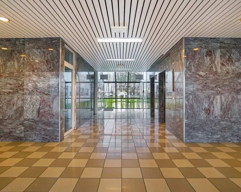 Ingangshal van een kantoorruimte aan de Haagse Schouwweg met marmeren wanden en grote ramen aan het einde van de gang.