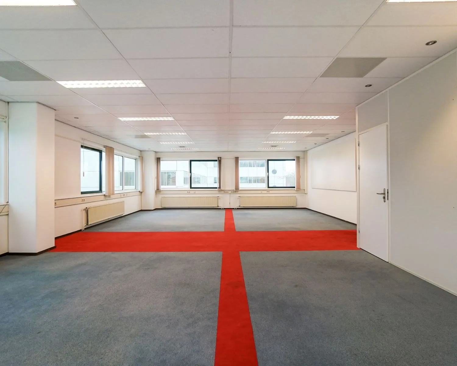 Lege kantoorruimte aan de Haagse Schouwweg met grijs tapijt en rood kruisvormig patroon op de vloer.