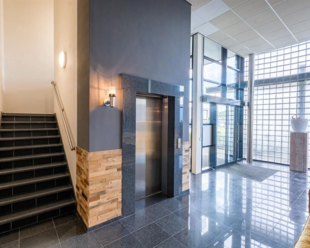 Moderne entreehal van een kantoorpand aan de Mollerusweg 84 met lift, trap en glazen gevel.