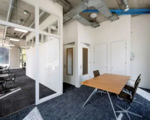 Moderne kantoorruimte aan de Oostenburgermiddagstraat 601 met glazen wanden, industriële plafonds en een vergadertafel met stoelen.