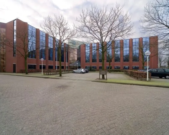 Modern rood-bruin kantoorgebouw met spiegelramen aan de Pascalstraat 15, met parkeerplaatsen en bomen op de voorgrond.