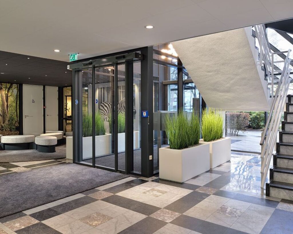 Moderne entreehal van kantoorpand aan de Pascalstraat 15 met glazen draaideur, plantenbakken en trap naar boven.