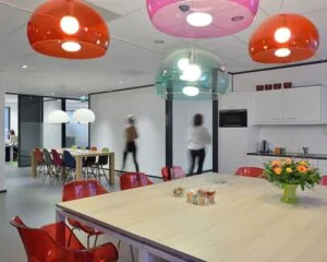 Moderne kantoorruimte aan de Pascalstraat 15 met kleurrijke stoelen, hanglampen en een gezamenlijke keukentafel.