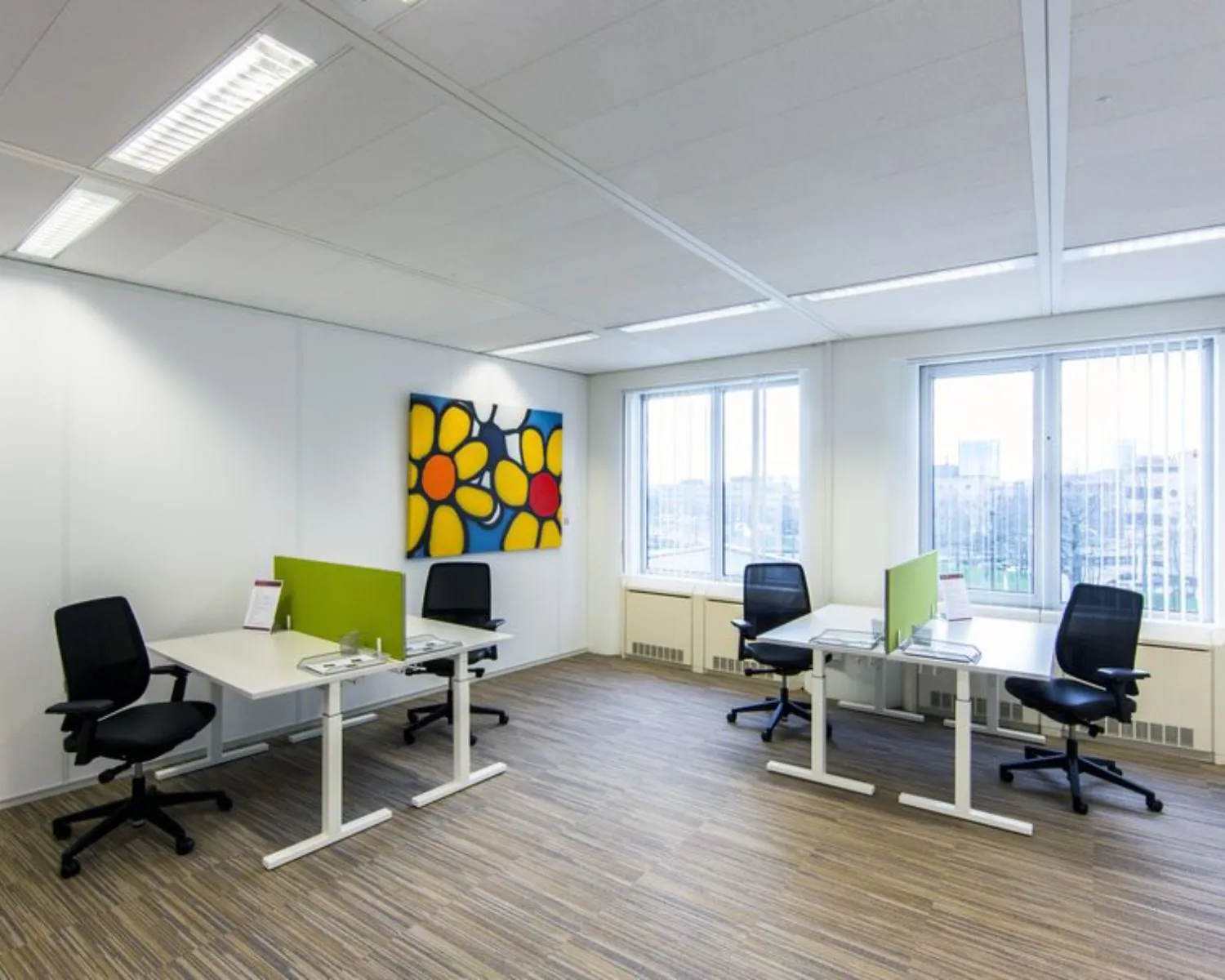 Moderne kantoorruimte met vier werkplekken, grote ramen en een kleurrijk schilderij aan de muur aan de Polarisavenue 1 in Hoofddorp.