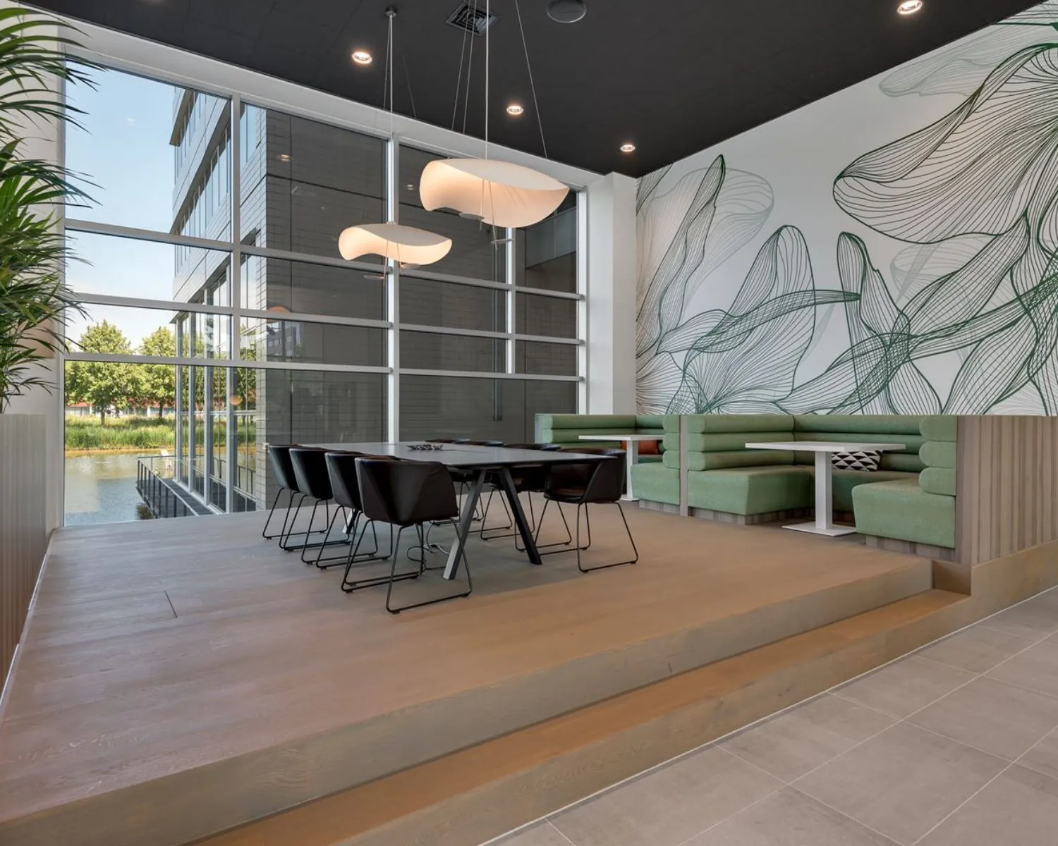 Moderne kantoorruimte aan de Polarisavenue 1 in Hoofddorp met grote ramen, vergadertafel, groene zithoeken en abstracte muurtekening.