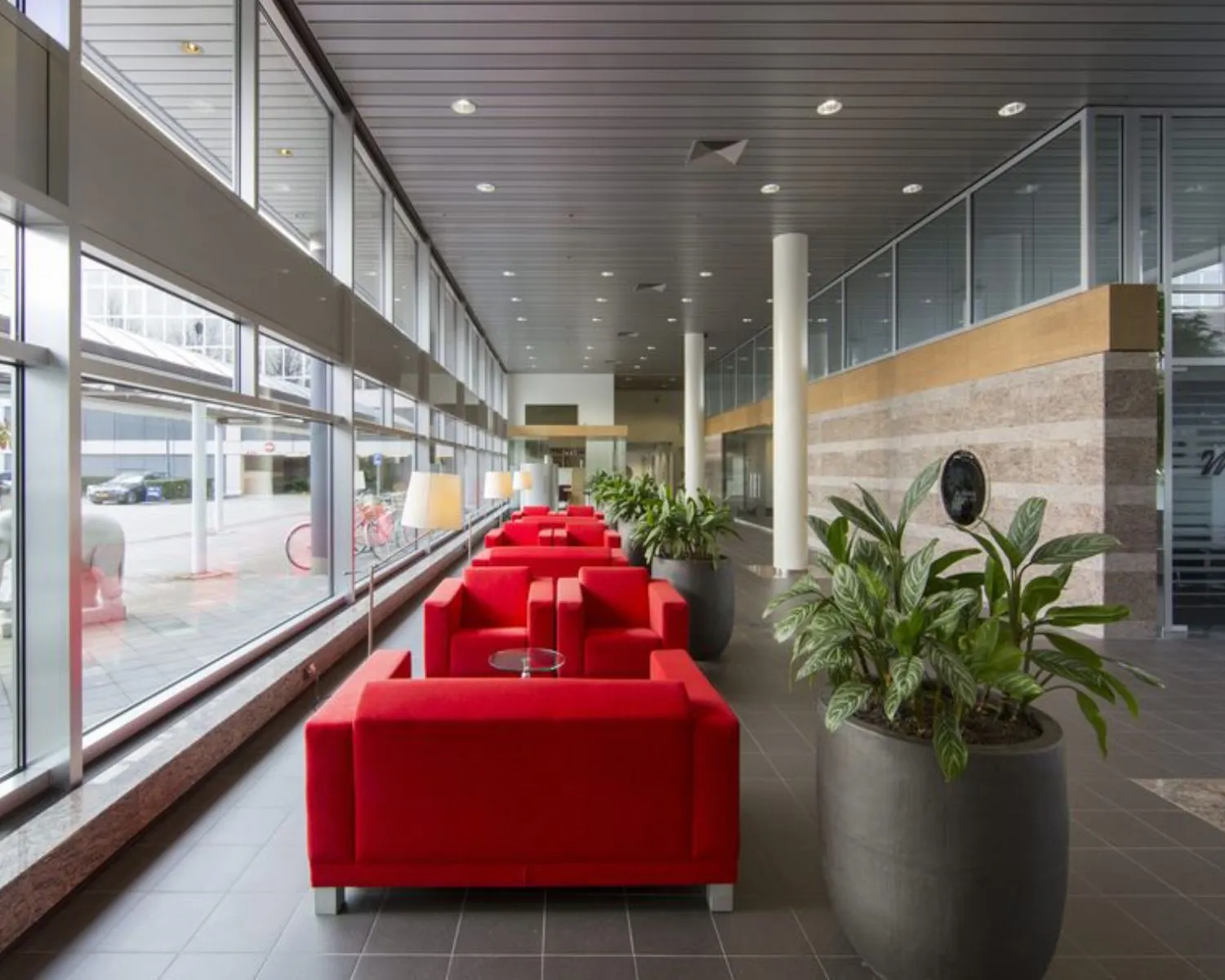 Moderne kantoorlobby aan de Polarisavenue 1 in Hoofddorp met rode zitbanken, grote planten en hoge ramen.