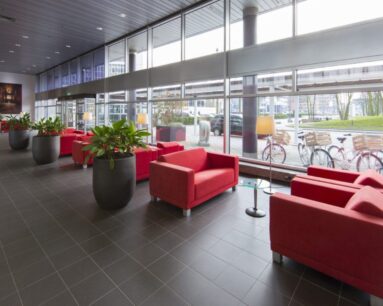 Moderne wachtruimte met rode zitbanken, grote planten en veel daglicht in een kantoorpand aan de Polarisavenue in Hoofddorp.