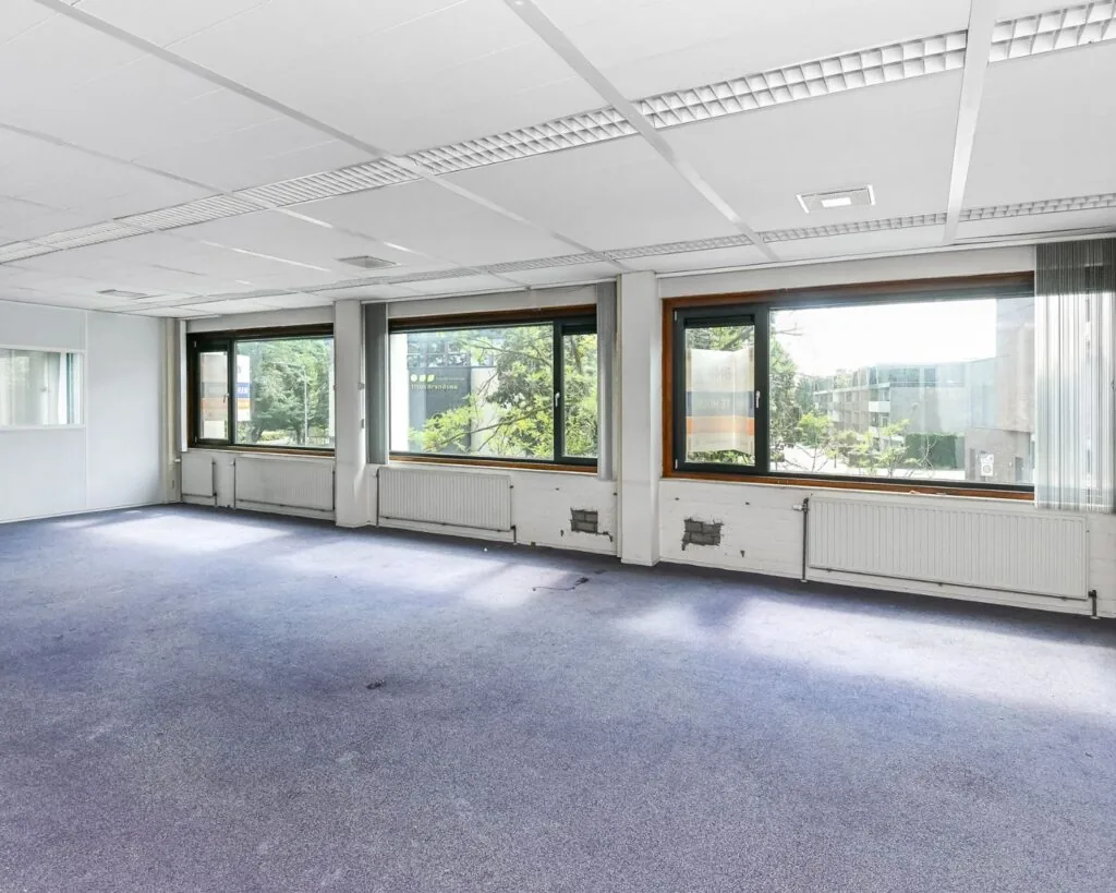 Lege kantoorruimte met grote ramen en paarse vloerbedekking aan de Reigerstraat 30.