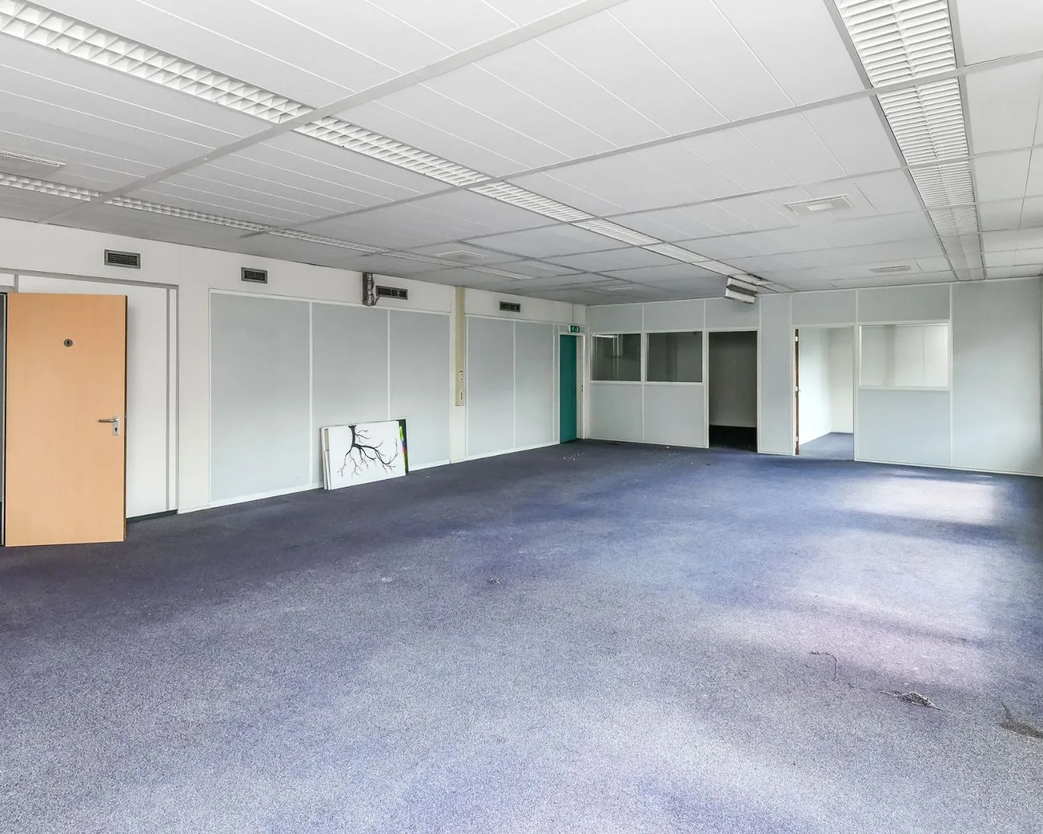 Lege kantoorruimte met blauw tapijt, systeemplafond en meerdere glazen scheidingswanden aan de Reigerstraat 30-6.