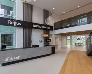 Moderne ontvangsthal van een kantoorpand aan de Saturnusstraat 46 in Hoofddorp met een balie en bedrijfsnamen zoals Regus en Buma/Stemra.