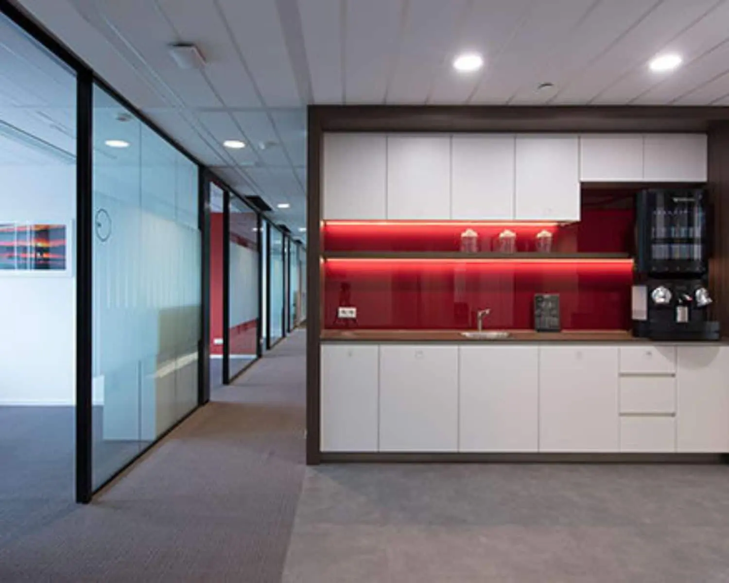 Moderne pantry met witte kasten en rode achterwand in een kantoorruimte aan de Saturnusstraat 46 in Hoofddorp.