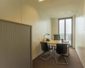 Kleine kantoorruimte te huur aan Stationsplein 8-15 met bureau, stoelen en uitzicht op de stad.