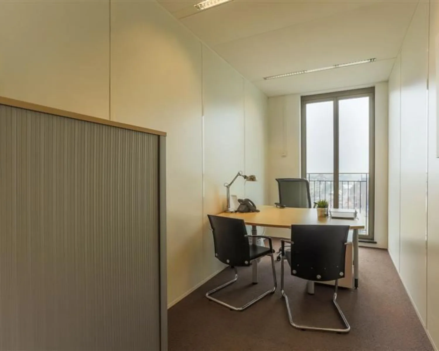 Kleine kantoorruimte te huur aan Stationsplein 8-15 met bureau, stoelen en uitzicht op de stad.