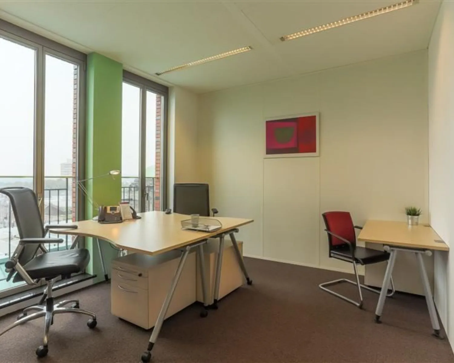 Moderne kantoorruimte te huur aan het Stationsplein 8-16 met twee bureaus, stoelen en grote ramen met uitzicht.