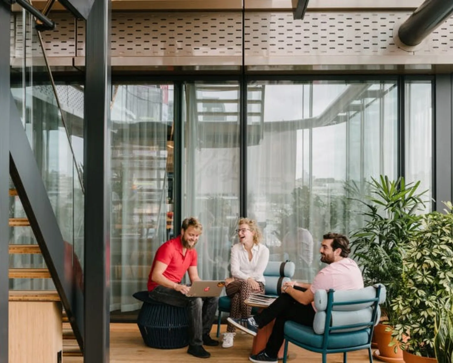 Moderne kantoorruimte aan de Strawinskylaan met drie mensen in overleg bij een glazen wand en omringd door planten.