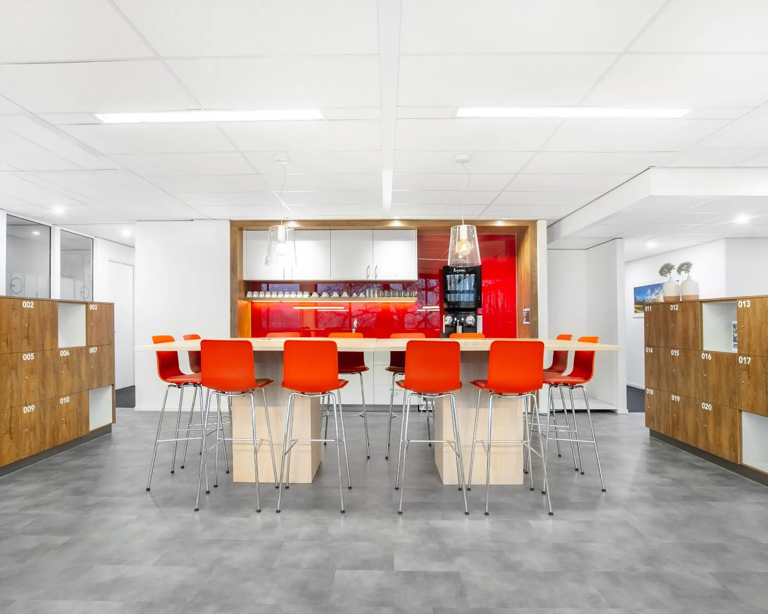 Moderne pantryruimte in een kantoor aan de Laan van Westroijen 6 in Tiel, met hoge tafels, feloranje stoelen en een rode achterwand.