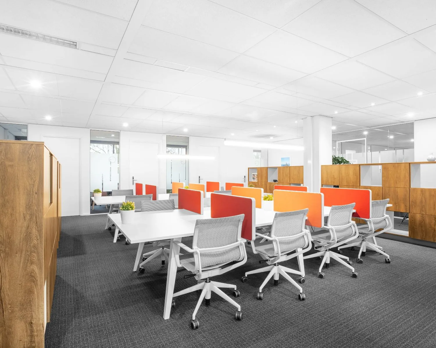 Moderne kantoorruimte in Tiel met flexwerkplekken, oranje scheidingspanelen en houten kasten.