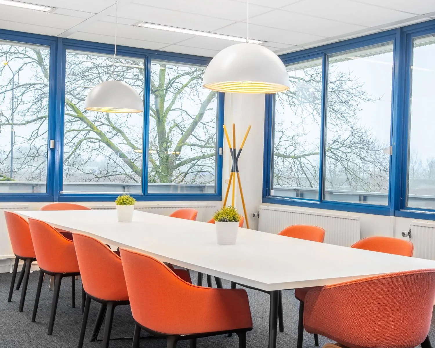 Moderne kantoorruimte in Tiel met een vergadertafel, oranje stoelen en grote ramen met uitzicht op bomen.