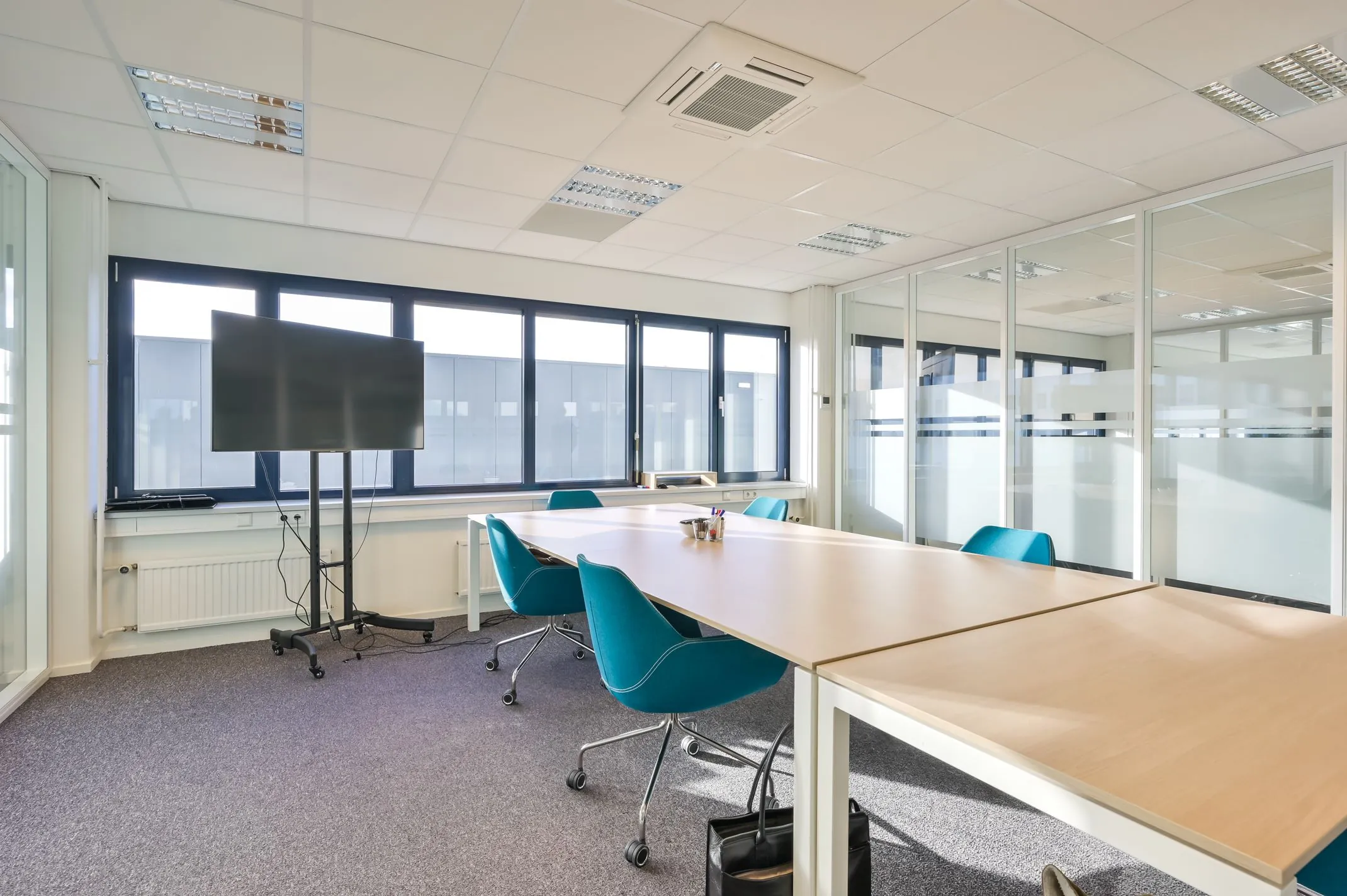 Moderne vergaderruimte met grote ramen, glazen wanden, een scherm en turquoise stoelen aan Kobaltweg 11.