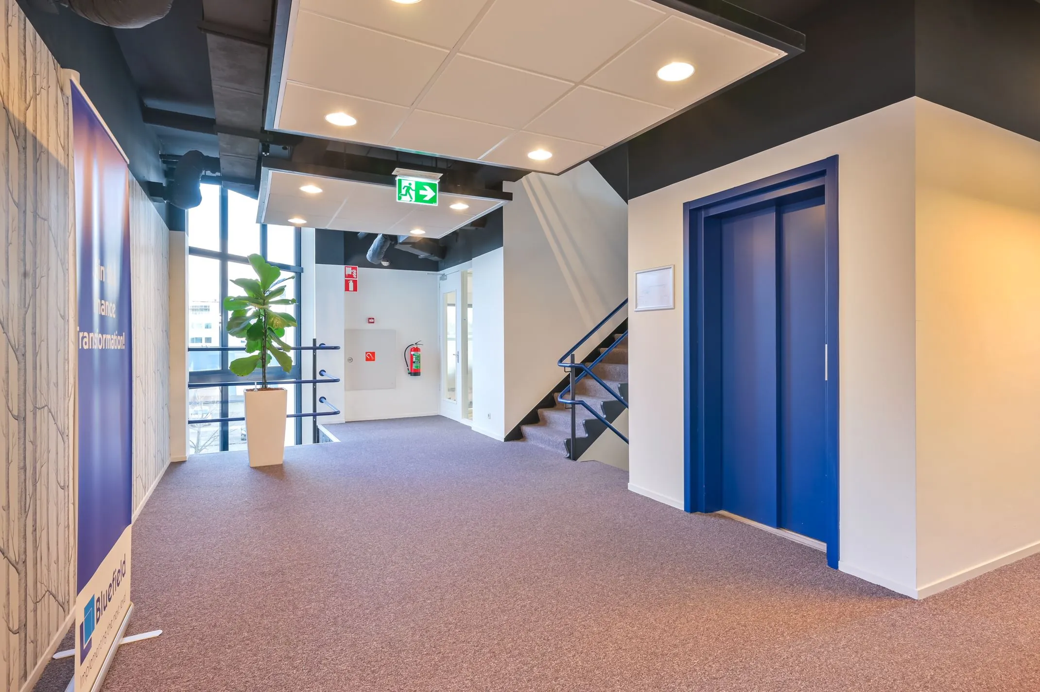 Moderne kantoorruimte aan de Kobaltweg 11 met blauwe liftdeuren, trapopgang en natuurlijk licht.