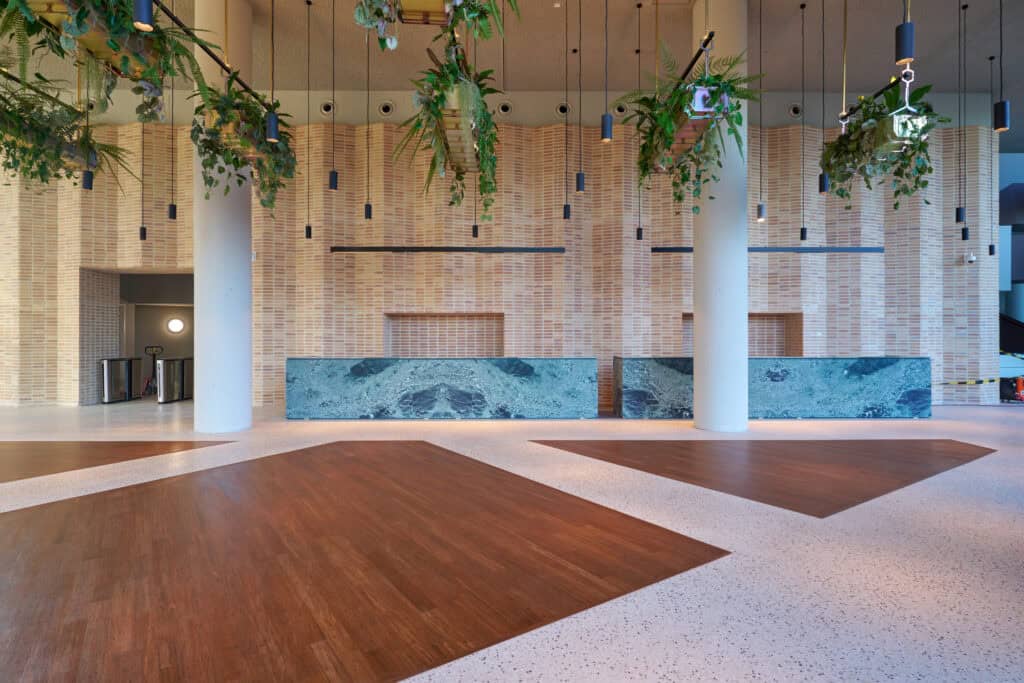 Moderne entreehal van een kantoorruimte aan de Hildegard von Bingenstraat 44 in Amsterdam met houten vloeraccenten, hangende planten en marmeren balies.