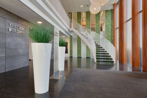 Moderne entree van het Chelsea Building in Rijswijk met een open trap, hoge plantenbakken en groene wandaccenten.