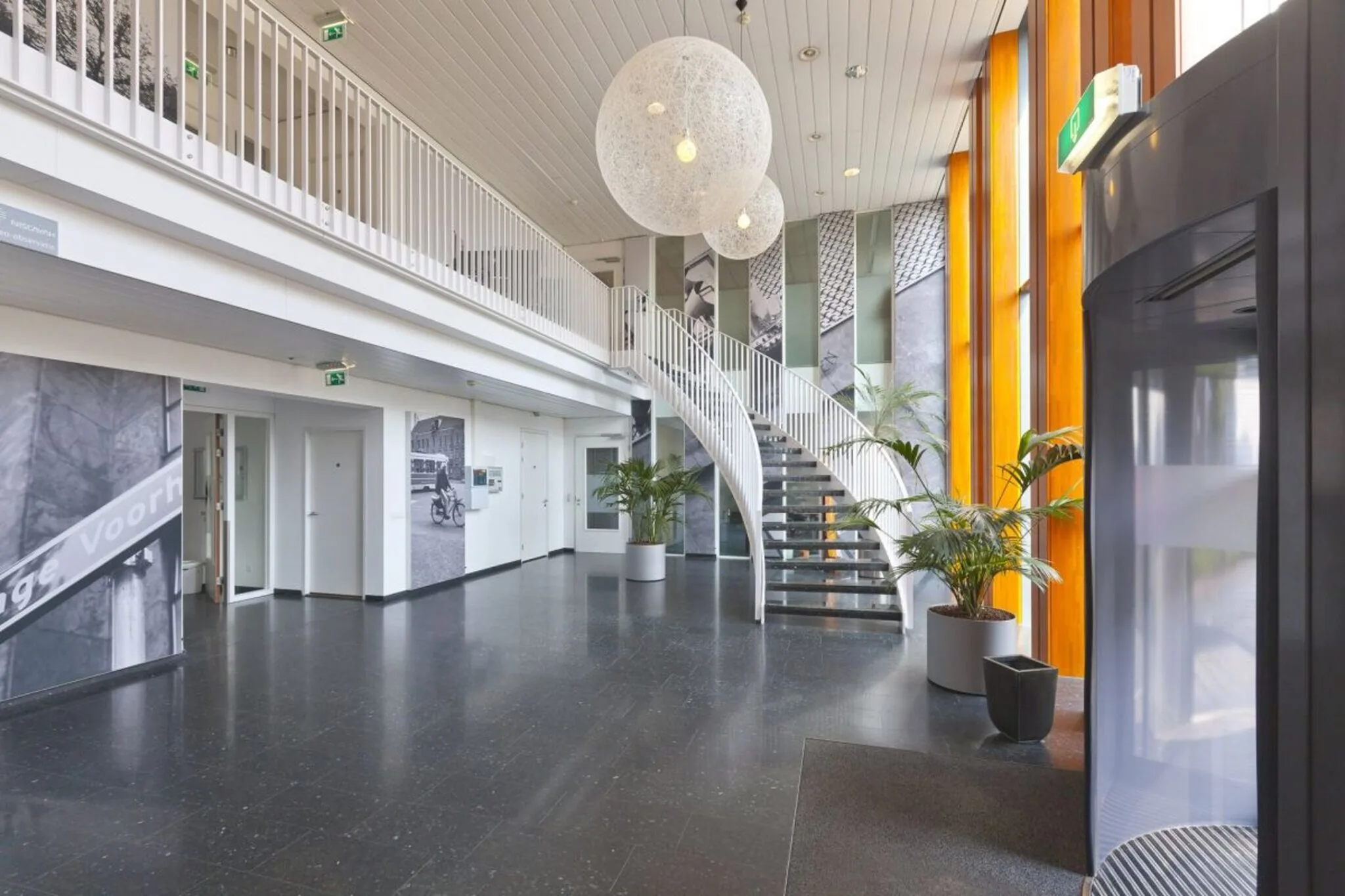 Moderne en lichte entreehal van een kantoorruimte in Rijswijk met een ronde trap, grote ramen en decoratieve hanglampen.