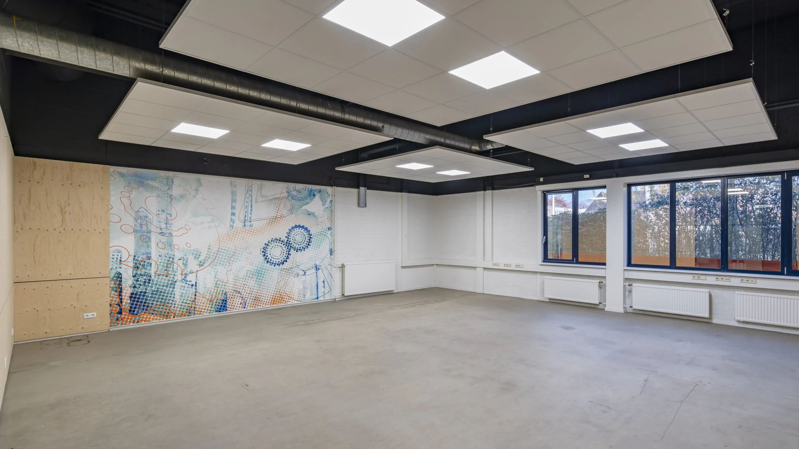 Leegstaande kantoorruimte aan de Tarasconweg 2 in Eindhoven met grote ramen en een kleurrijke muurschildering.