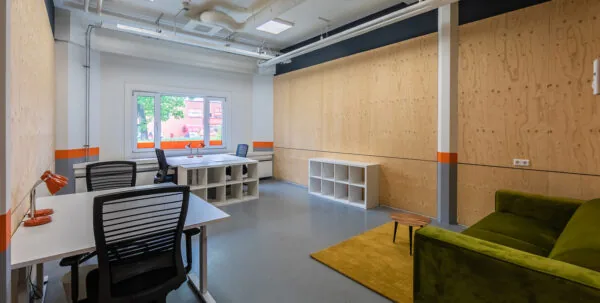 Moderne kantoorruimte in Aalsmeer met bureaus, stoelen, opbergrekken en een groene bank.