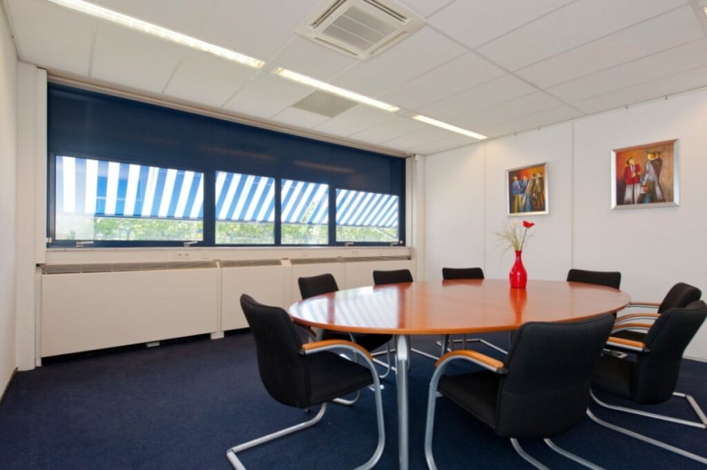 Vergaderruimte met ovale tafel, zes stoelen, grote ramen met zonwering en moderne kunst aan de muur in een kantoor aan de Markerkant 13-70 in Almere.