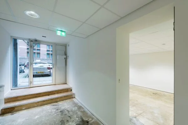 Inkomhal van een kantoorruimte aan de Jan Luijkenstraat 92 in Amsterdam, met glazen voordeur, traptreden en zicht op een lege kantoorruimte.
