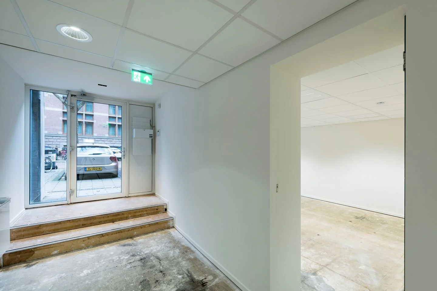 Inkomhal van een kantoorruimte aan de Jan Luijkenstraat 92 in Amsterdam, met glazen voordeur, traptreden en zicht op een lege kantoorruimte.